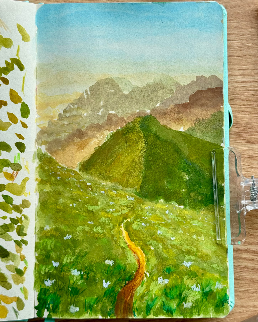 Painting of a mountain landscape in a notebook on a wooden surface