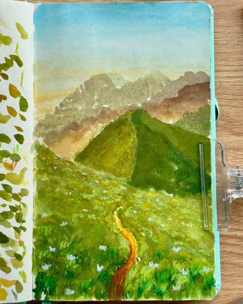 Painting of a mountain landscape in a notebook on a wooden surface